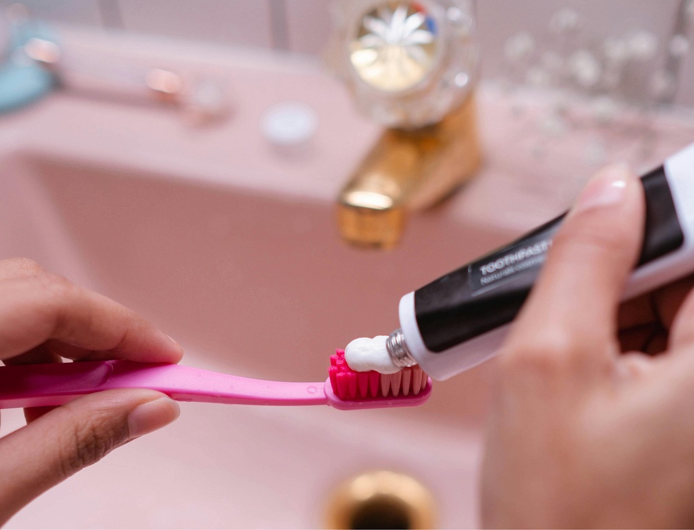 Persona aplicando pasta dental sobre un cepillo frente a un grifo cerrado, como ejemplo de ahorro de agua durante el cepillado de dientes.